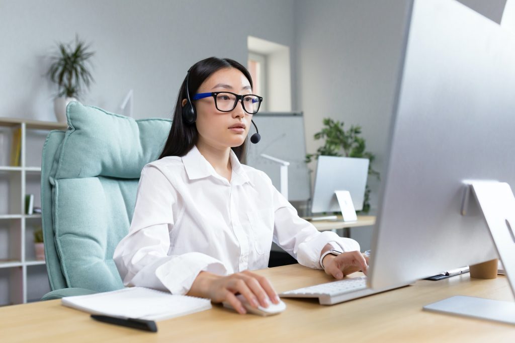 Online distance learning. Asian teacher in headphones sitting at a table teaching a lesson online