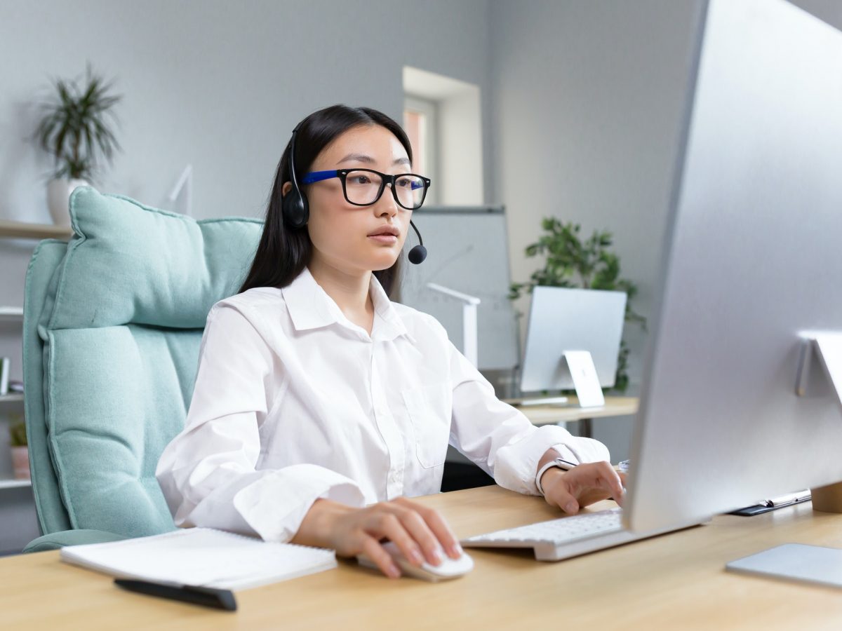 Online distance learning. Asian teacher in headphones sitting at a table teaching a lesson online