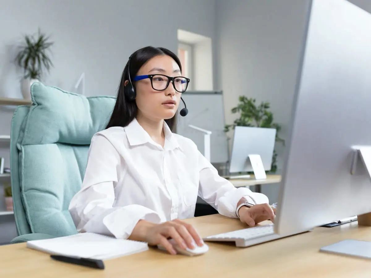 Online distance learning. Asian teacher in headphones sitting at a table teaching a lesson online