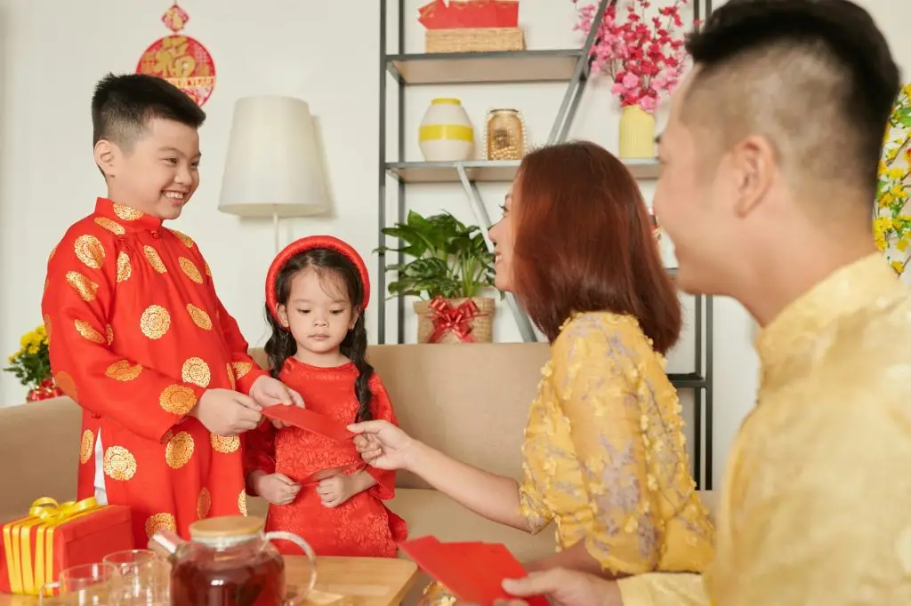 Parents handing red envelopes to a young girl in a red dress for Lunar New Year