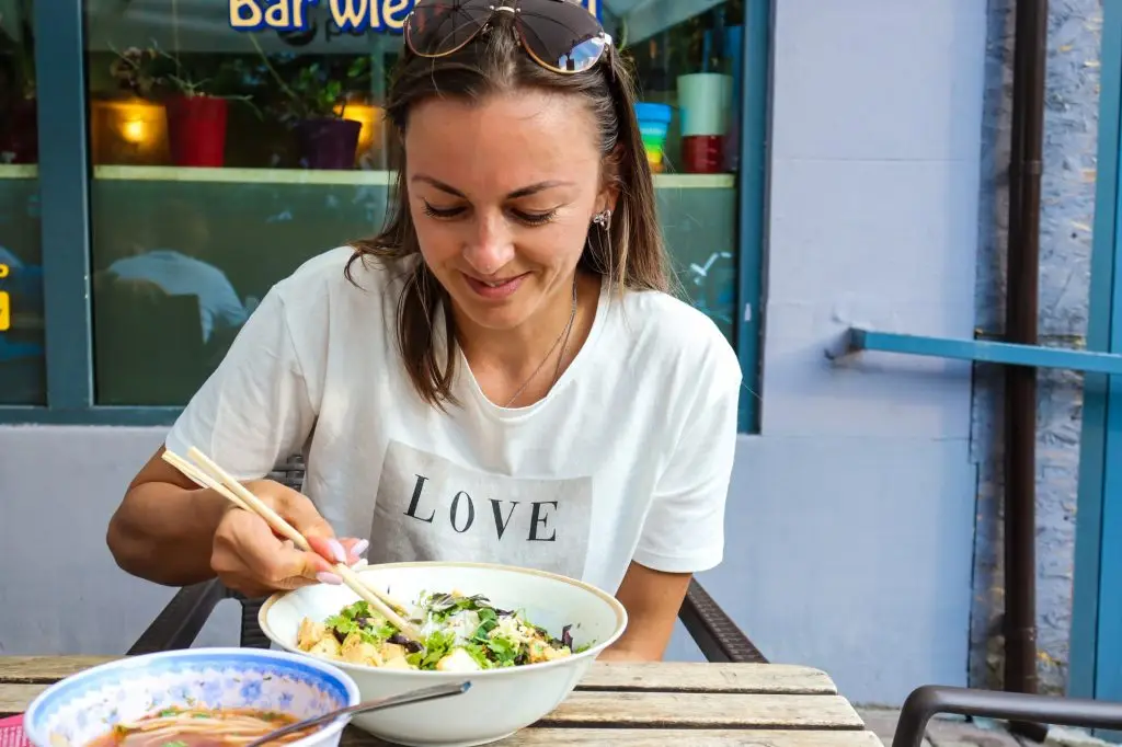 A woman is eating Chinese food outside the bar.