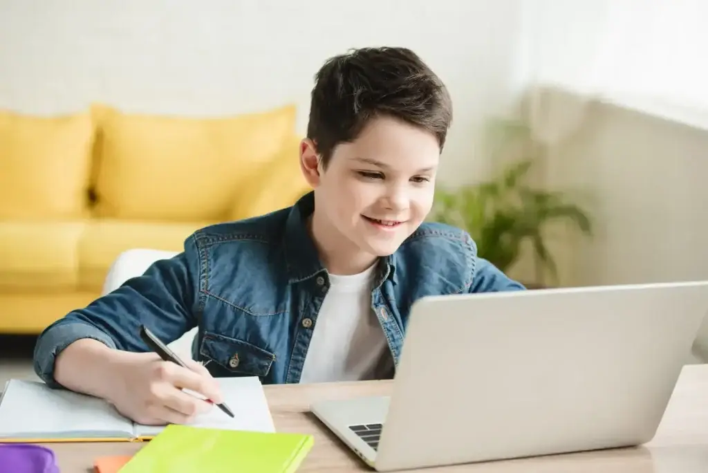 Boy writing notebook online tutoring laptop