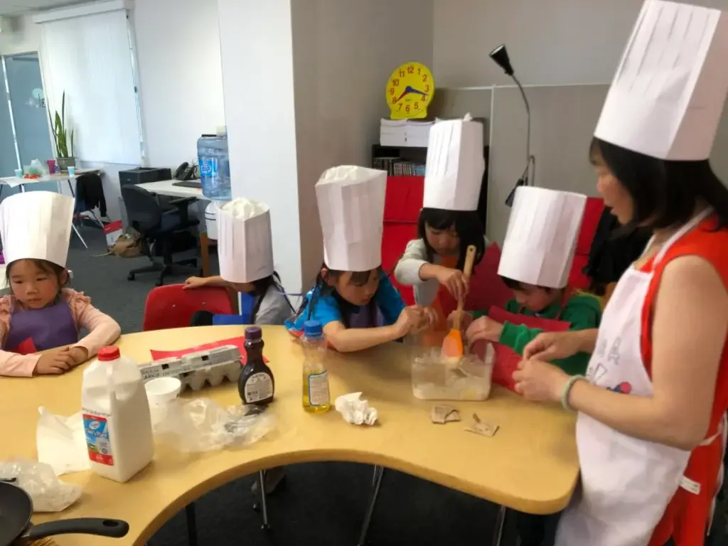 Mandarin summer camp students in paper chef hats during a cooking activity