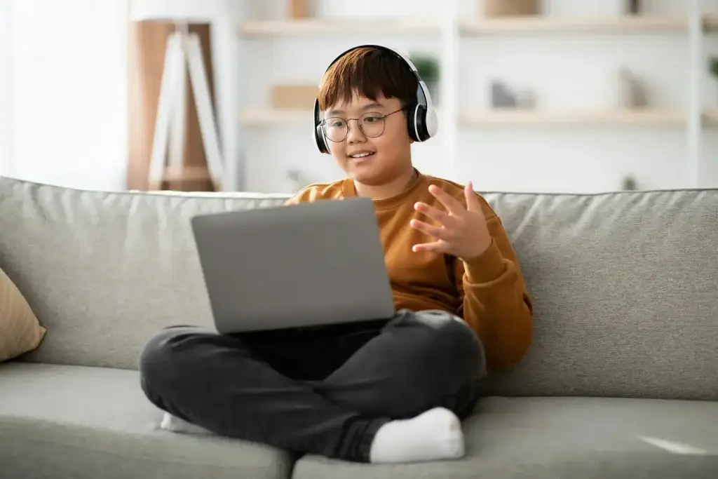 Teenager wearing headphones taking an online lesson on a laptop at home